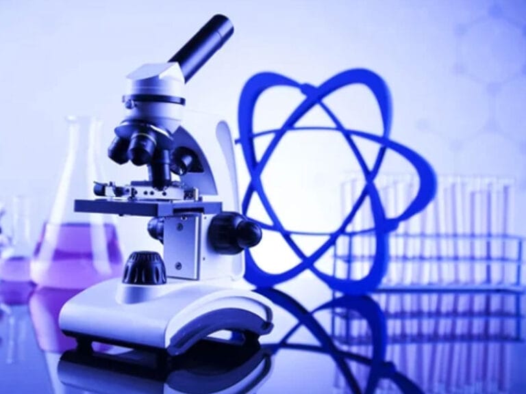 A microscope in a laboratory setting with a blue atomic model in the background. Laboratory glassware is visible, including test tubes and flasks.