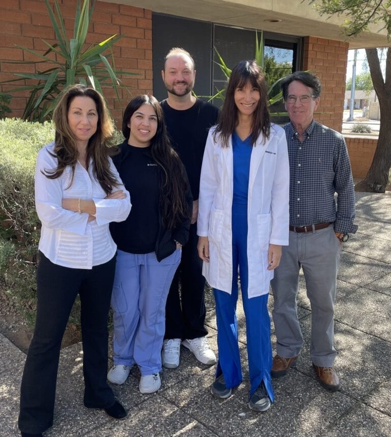 Five people stand together outside a building, with three people wearing medical attire.