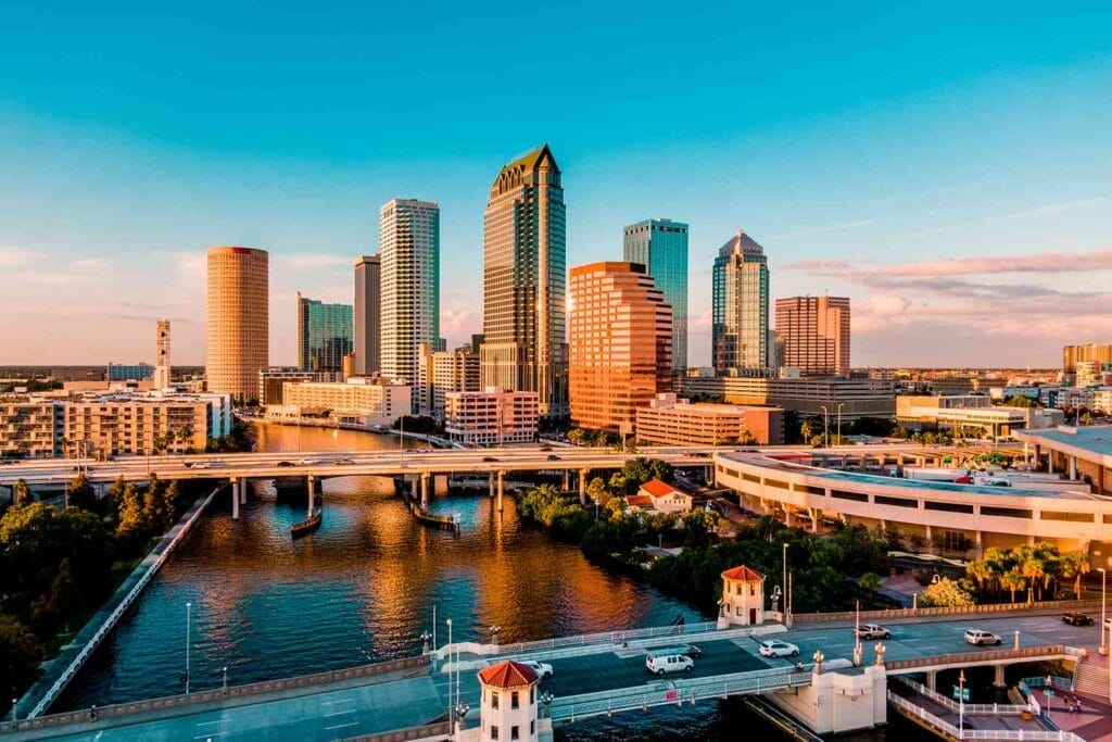 Aerial view of a city skyline with tall buildings under a clear blue sky, a river running through, and several bridges connecting different parts of the city.